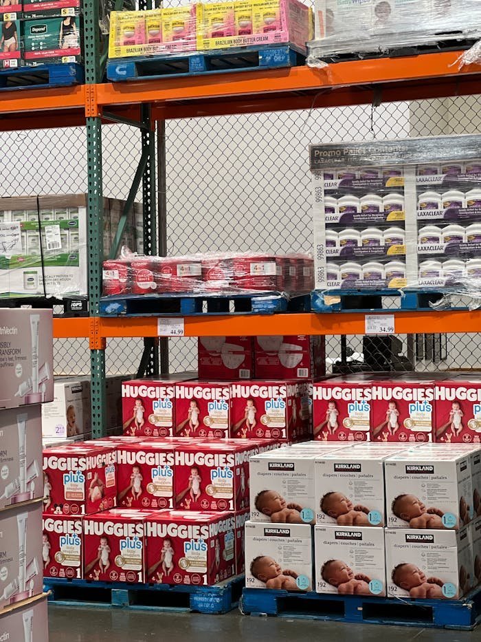 Stock photo of shelves filled with various baby diaper brands in a warehouse setting.
